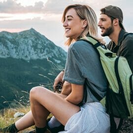 A male and female sitting at the peak of a mountain, enjoying the view of the mountain range.