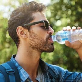 A man with sunglasses drinking some CBD water on a sunny day.