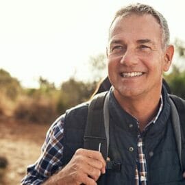A middle aged man smiling while hiking with a hiking backpack.