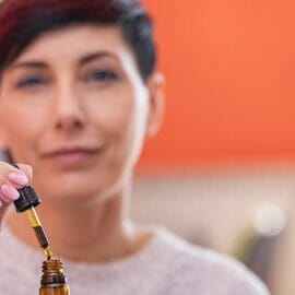 A woman holding the dropper-lid of a CBD bottle just above the bottle.