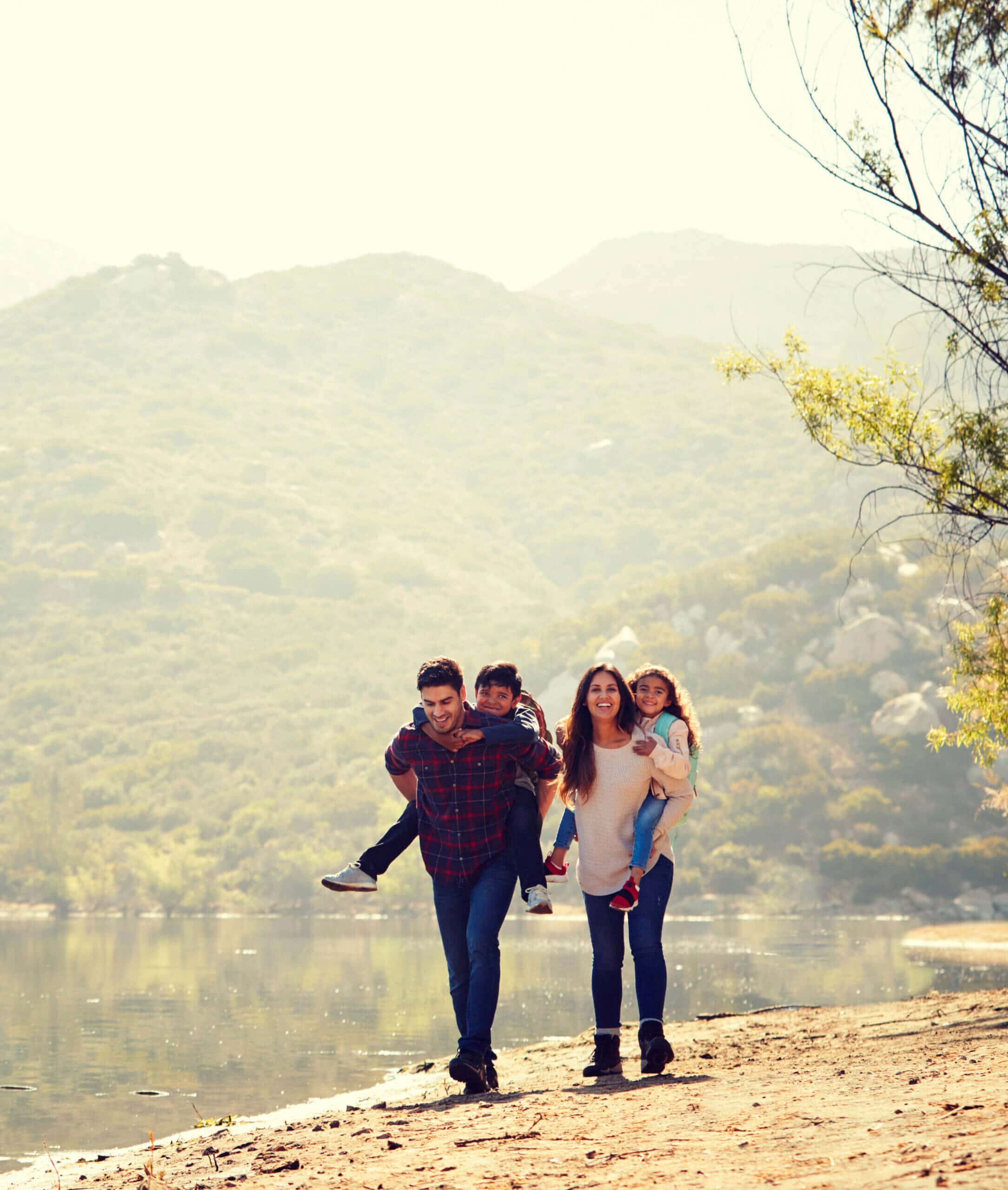 Parents piggybacking their young children by a mountain lake