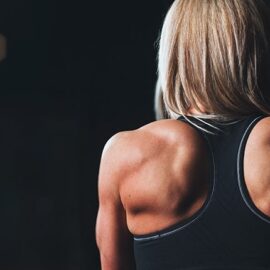 The flexed deltoid muscles of a woman in workout clothing.