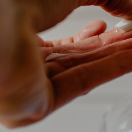 A hand about to press down on a hand sanitizer nozzle.