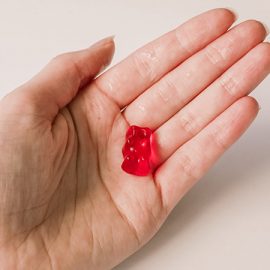 A single gummy bear, a CBD edible, in the palm of a hand against a white background.