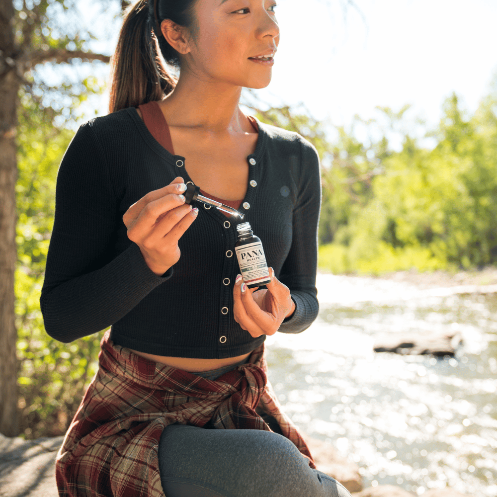 young woman holding tincture and dropper by river